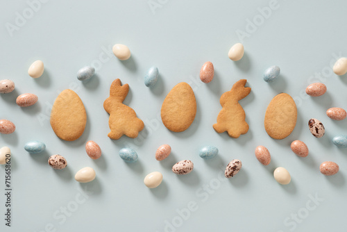 Easter glazed cookies shaped of bunny and chocolate sweets candy as eggs on blue background. View from above. Festive food and snacks. Greeting card.