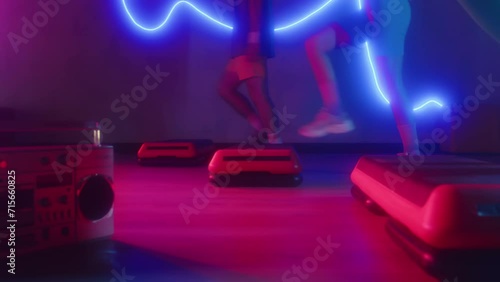 Cropped shot of active sportspeople practicing aerobics steps to boombox music in neon studio photo