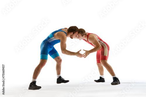 Young athlete man, wrestlers in blue and red uniform hand wrestling in neutral position on their feet against white studio background. Concept of sport, mixed martial arts, active lifestyle, movement.