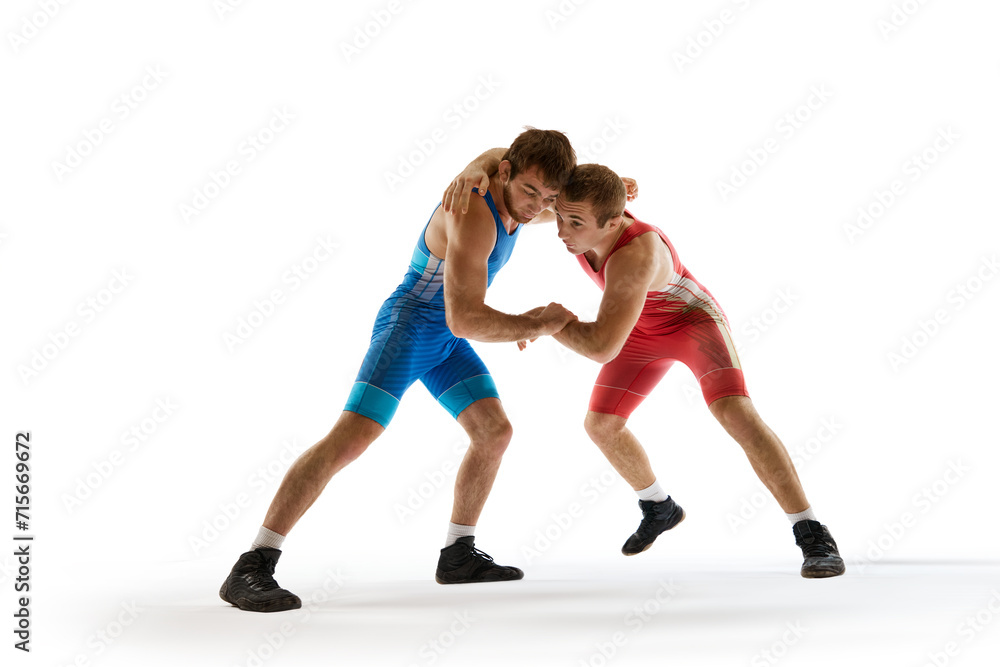 Young athlete man, wrestlers in blue and red uniform hand wrestling in motion against white studio background. Concept of sport, mixed martial arts, active lifestyle, movement. Ad