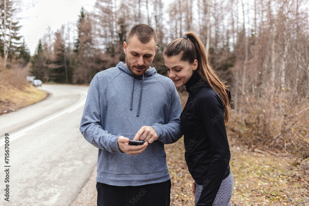 Fototapeta premium Two young people checking their fitness progress on a smartphone app after a morning run.
