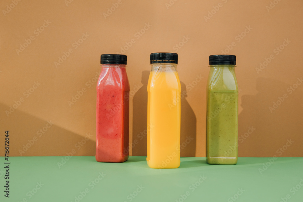 Fruit and vegetable smoothies in transparent plastic bottles. Red, green, orange smoothies on a brown-green background. The concept of healthy eating. Front view Fruit and vegetable smoothies in transparent plastic bottles. Red, green, orange smoothies on a brown-green background. The concept of healthy eating. Front view