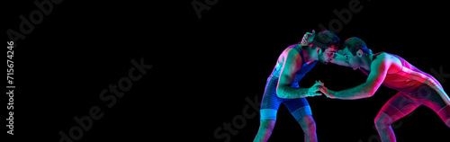 Banner. Two freestyle wrestlers hand fighting in mixed neon lights against black background with negative space to insert text. Concept of fair wrestling, championship, win competition.