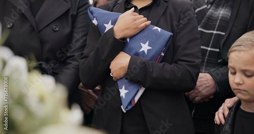 Funeral, cemetery and woman with American flag for veteran for respect, ceremony and memorial service. Family, depression and sad people by coffin in graveyard for military, army and soldier mourning photo