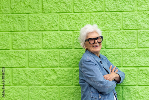 elderly lady in denim jacket standing against a lime green wall photo