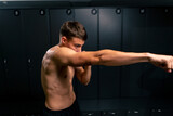 young guy kickboxer with a pumped up body practices punches in the locker room in gym muscle relief