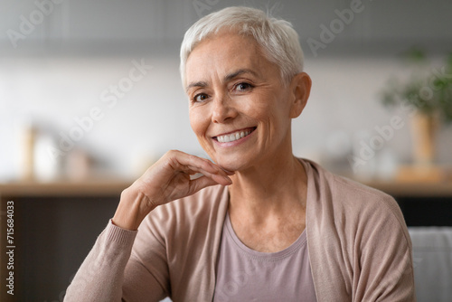 Cheerful elderly woman looking at camera with warm smile indoor