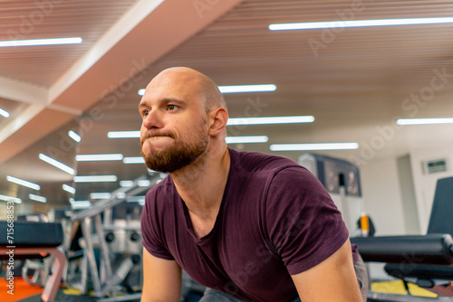 stressed face of a bodybuilder doing strength exercises with a barbell in the gym during sports