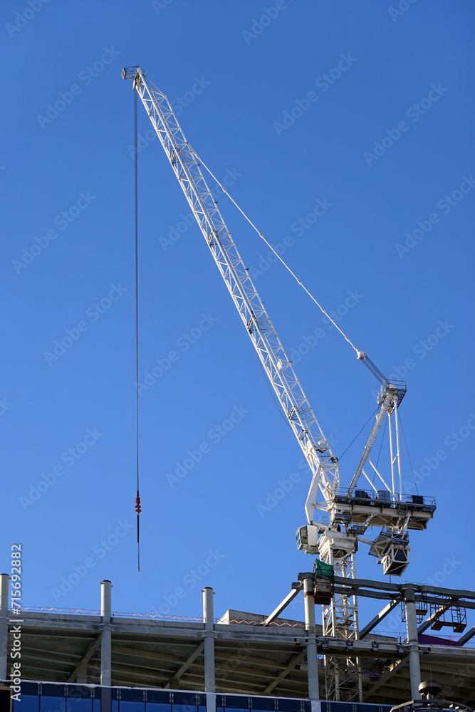 Hoisting tower crane on the top section being constructed of modern high skyscraper building against blue cloudless sky