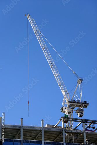 Hoisting tower crane on the top section being constructed of modern high skyscraper building against blue cloudless sky