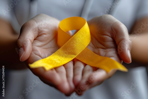 Yellow ribbon in hands, blurred background for supporting World Cancer Day campaign