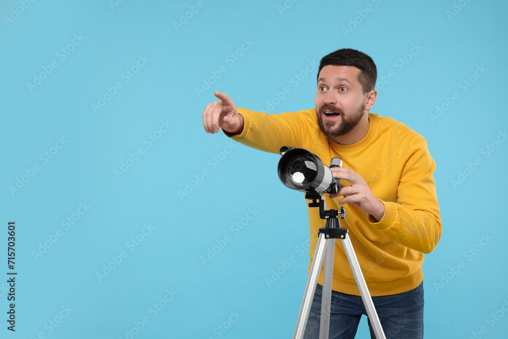 Obraz premium Happy astronomer with telescope pointing at something on light blue background. Space for text