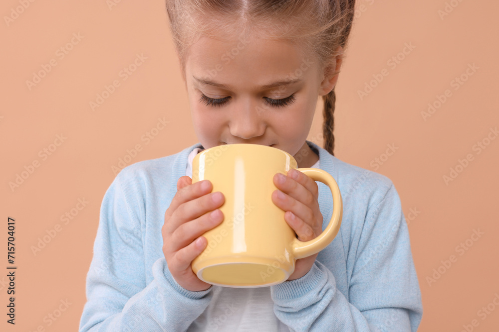 Cute girl drinking beverage from yellow ceramic mug on beige background Cute girl drinking beverage from yellow ceramic mug on beige background