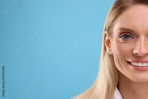 Portrait of smiling middle aged woman on light blue background, closeup. Space for text