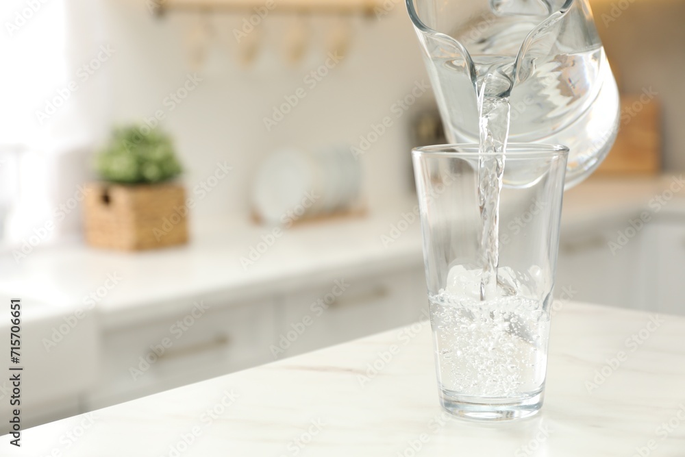 Pouring water from jug into glass on white table in kitchen. Space for text Pouring water from jug into glass on white table in kitchen. Space for text