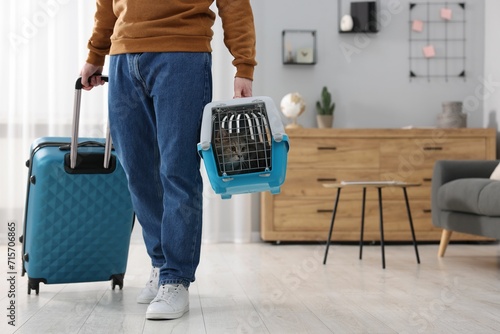Travel with pet. Man holding carrier with cute cat and suitcase at home, closeup. Space for text photo