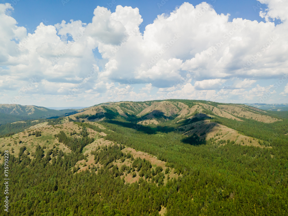 Fototapeta premium A beautiful sunrise landscape. Aerial view beautiful mountains covered with green pine forest against a background of blue sky with white clouds. Nature background. Photo from the drone.