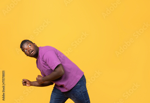 Scared black man bending down in defensive pose, yellow backdrop photo