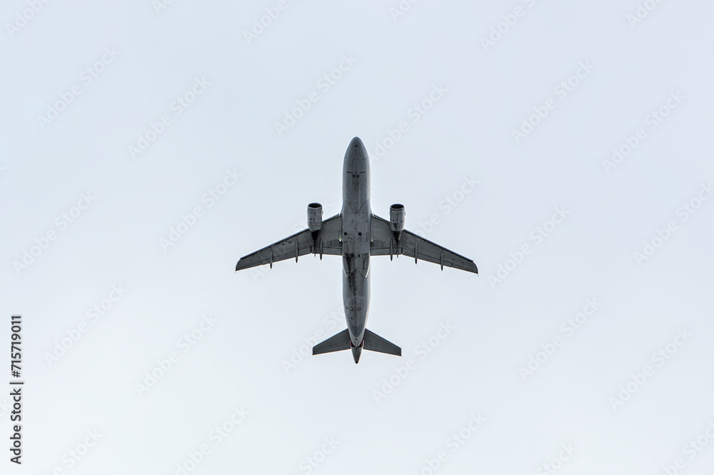 Obraz premium airplane flying through clouds (seen from below in dark silhouette against bright blue sky) shadow, outline of commercial airline plane seen from the ground
