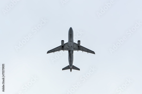 airplane flying through clouds (seen from below in dark silhouette against bright blue sky) shadow, outline of commercial airline plane seen from the ground