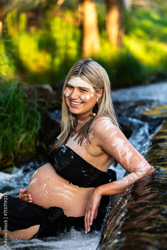 Pregnant Aboriginal lady in traditional ochre body paint sitting in waterfall in bushland Pregnant Aboriginal lady in traditional ochre body paint sitting in waterfall in bushland