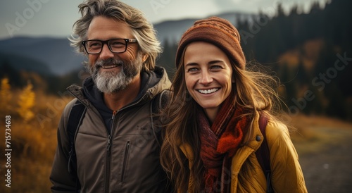 Amidst the crisp autumn air, a man and woman share a joyous moment captured in a portrait, their smiling faces framed by rugged mountains and bundled in cozy jackets and scarves, exuding warmth and l