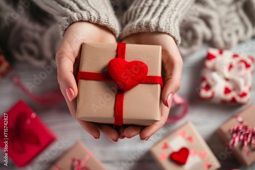 Capture a close-up of female hands cradling a gift, suitable for Valentine's Day, birthdays, and Mother's Day--an embodiment of love. Set against a Valentine's Day backdrop adorned with various gift b