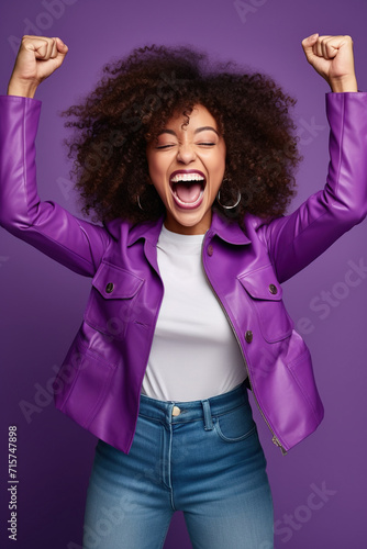 Overjoyed cheerful African American woman dressed stylish clothes celebrate success raise hands fists isolated on purple color background