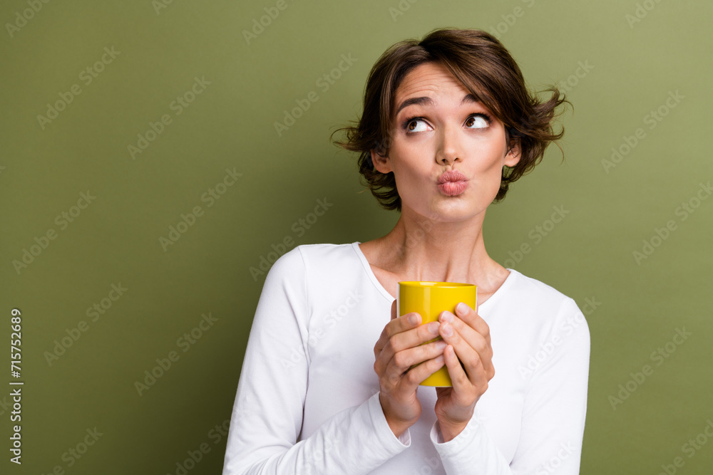 Photo portrait of lovely young lady hold mug pouted lips look empty space dressed stylish white garment isolated on khaki color background Photo portrait of lovely young lady hold mug pouted lips look empty space dressed stylish white garment isolated on khaki color background