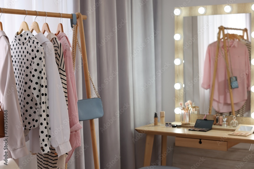 Makeup room. Clothes rack and stylish mirror with light bulbs on dressing table indoors