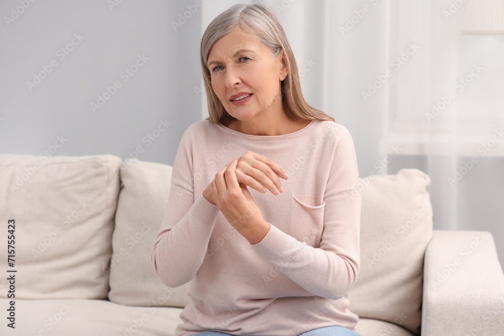 Mature woman suffering from pain in hand on sofa at home. Rheumatism symptom Mature woman suffering from pain in hand on sofa at home. Rheumatism symptom