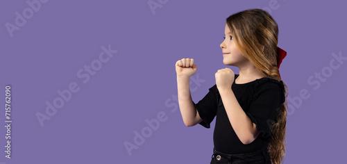 Horizontal picture of a little blonde girl dressed in black clothes in a fighting position, the concept of fighting training for children on a purple background.