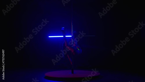 Woman doing erotic dance in dark studio coed by blue and red flashing light. Tight woman in yellow reflective lingerie practicing pole dance. photo