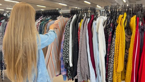 Selection of used clothes in a second-hand store. A woman buys inexpensive clothes photo
