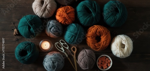  a group of balls of yarn sitting on top of a wooden floor next to a cup of teal and a teal colored crochel with a lit candle.