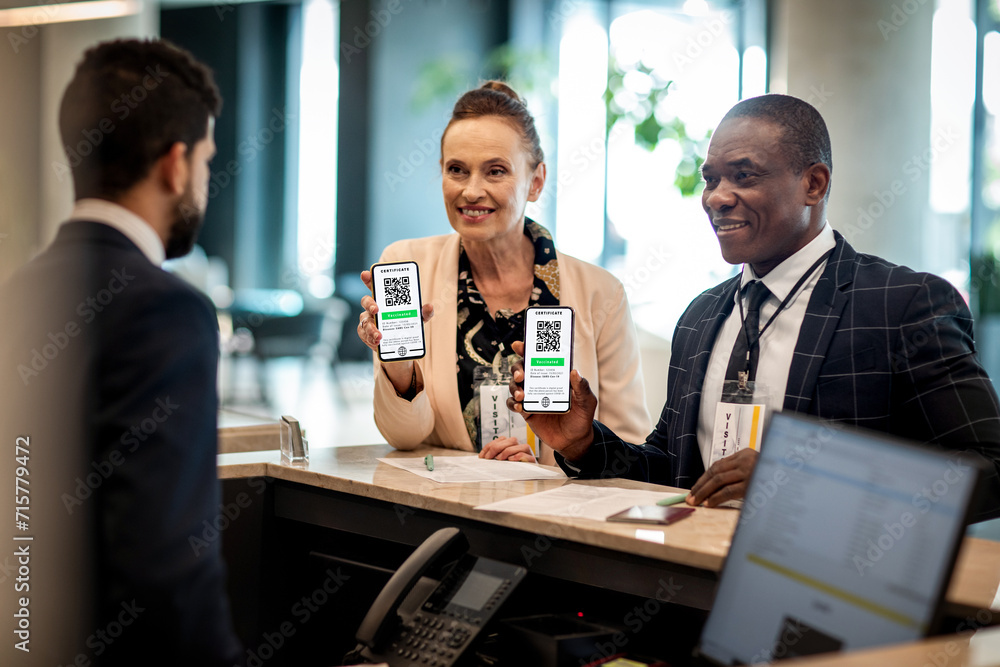 © Marko Geber - Diverse business people showing vaccine certificate to hotel reception