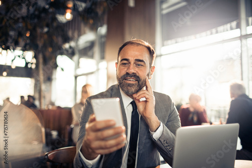 Smiling businessman using smartphone and laptop at cafe photo