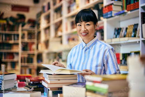 Portrait of a smiling Asian woman in the library, reading a book.