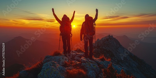 Hikers with arms raised up on mountaintop celebrating success at breathtaking sunrise