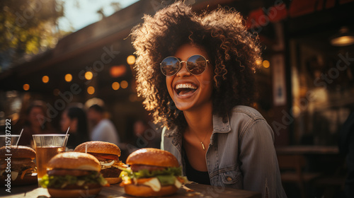 Young girl eating classic burger with friends at cafe in the city. Smiling beautiful young happy woman eating fast food.  photo