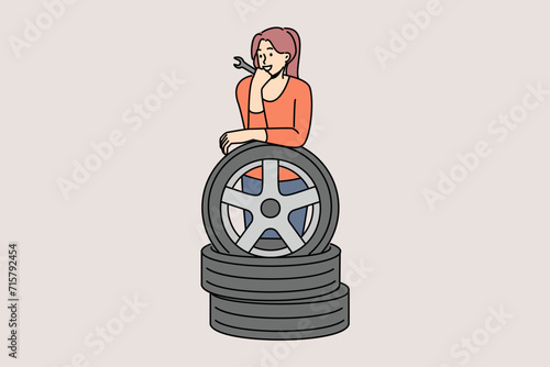 Woman auto mechanic prepares to replace car wheels during vehicle maintenance or repair. Happy girl auto mechanic with wrench in hands leans on tires, rejoicing at possibility replacing them on own