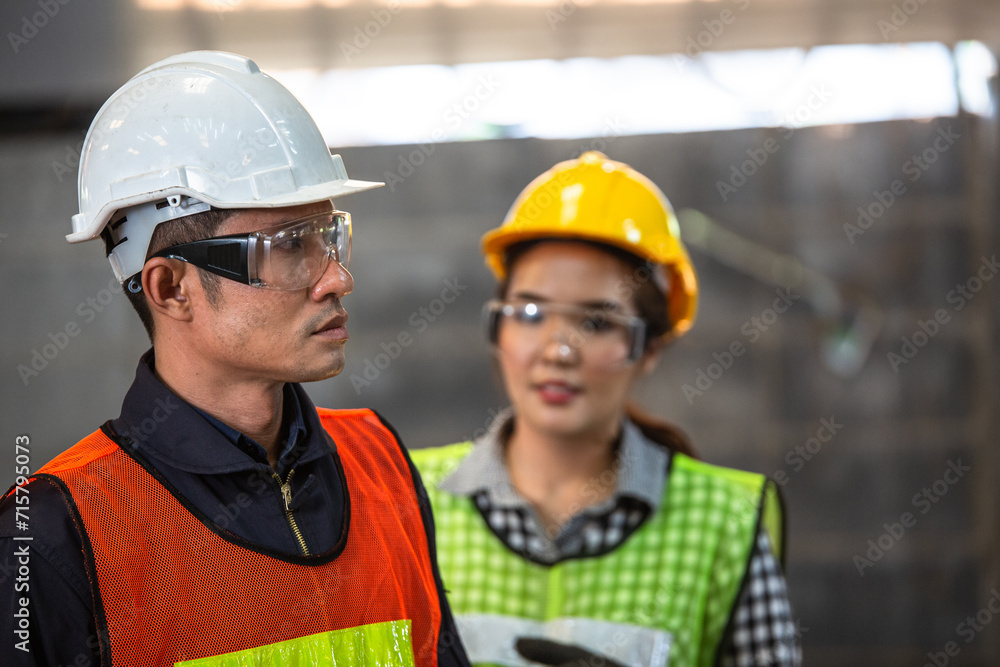 Asian engineer foreman wearing protective eyewear standing with female assistant at the construction site. Asian engineer foreman wearing protective eyewear standing with female assistant at the construction site.