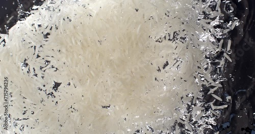 Super slow motion of dry basmati quality white rice is falling in pot with boiling water to be cooked with traditional recipes for dietetic vegetarian dish preparation by chef in restaurant kitchen. photo