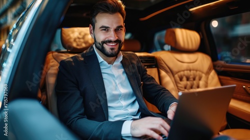 Handsome businessman working on laptop computer while sitting in luxury car. © Oulaphone