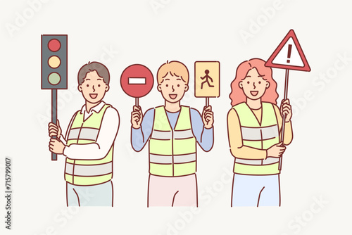 Traffic controllers urge young children to be careful while driving, holding road signs in hands