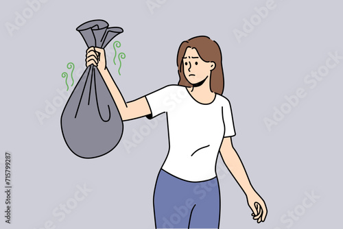 Woman with bag of smelly garbage in hands carries waste into trash can and feels disgusted because of bad smell. Girl throws out organic waste in dark plastic bags, not wanting to sort garbage.