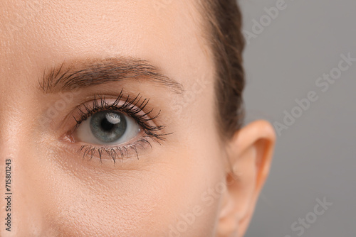 Woman with long eyelashes after mascara applying against grey background, closeup
