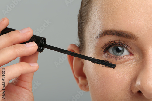 Woman applying mascara on grey background, closeup photo
