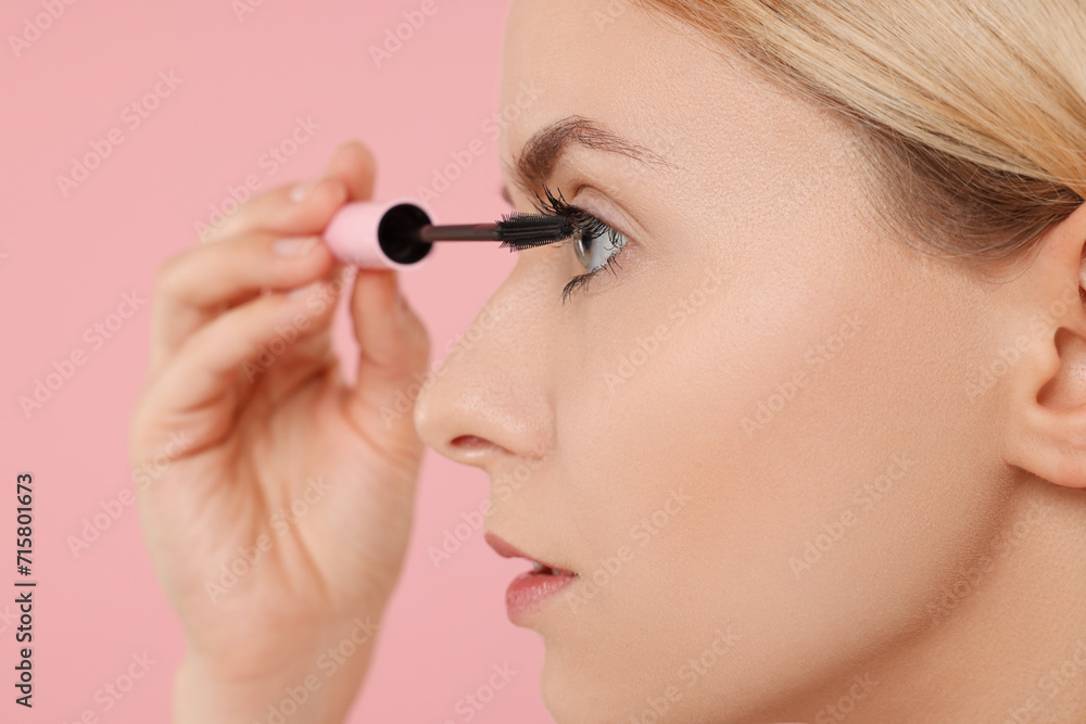 Beautiful woman applying mascara on pink background, closeup