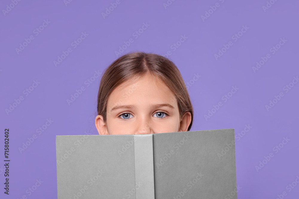 Cute schoolgirl with open book on violet background Cute schoolgirl with open book on violet background